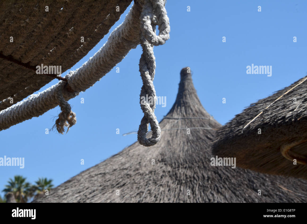 Thatched sun canopies on Coral Bay Beach, with hanging ropes Stock Photo