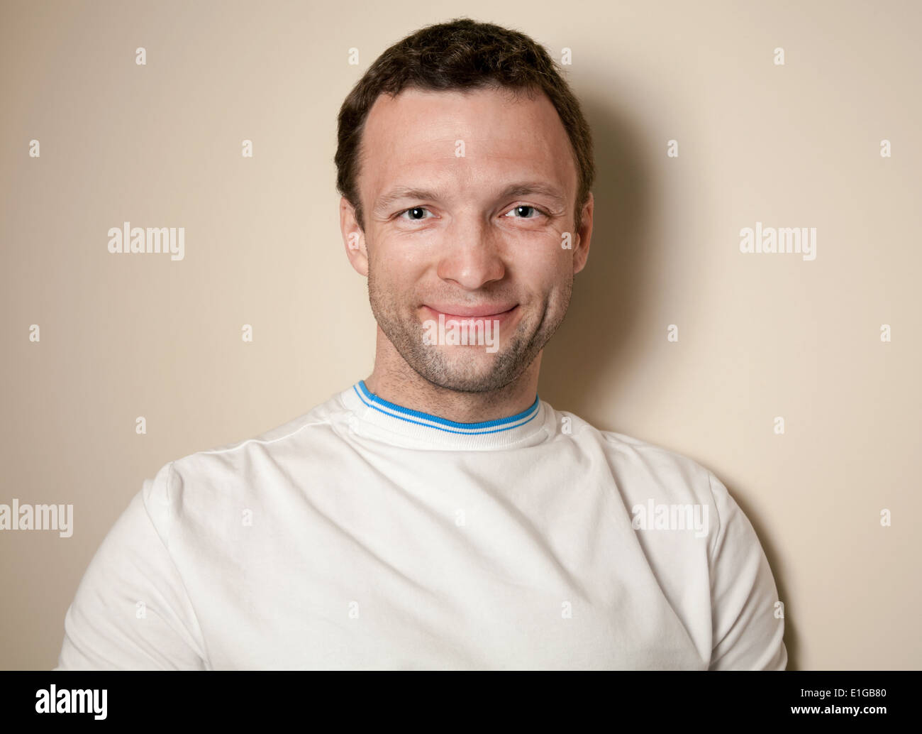 Smiling young Caucasian man in white t-shirt above gray wall Stock Photo
