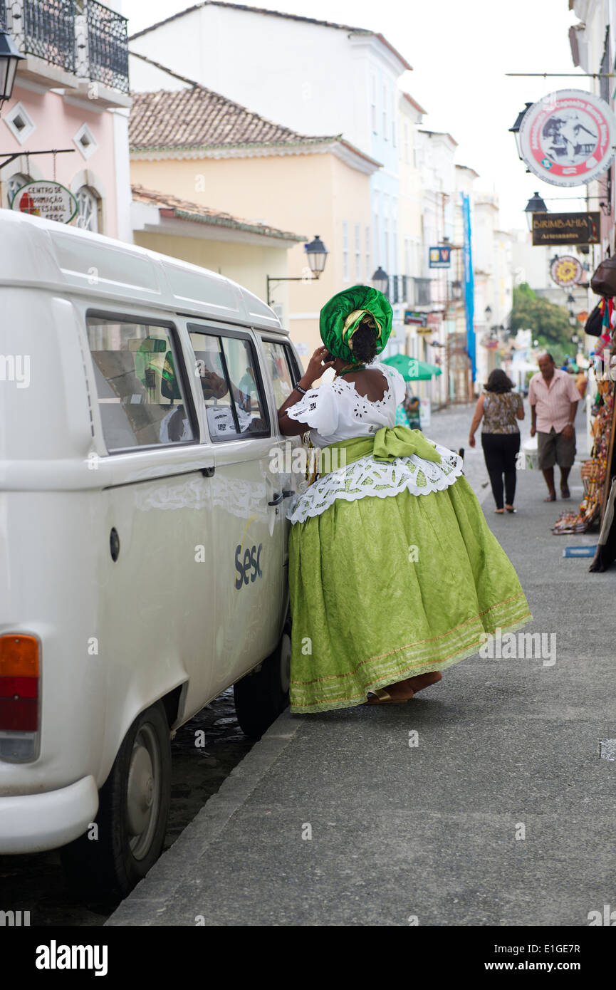 SALVADOR, BRAZIL - OCTOBER 15, 2013: Woman in traditional Baiana costume stands leaning on a Volkwagen Kombi. Stock Photo