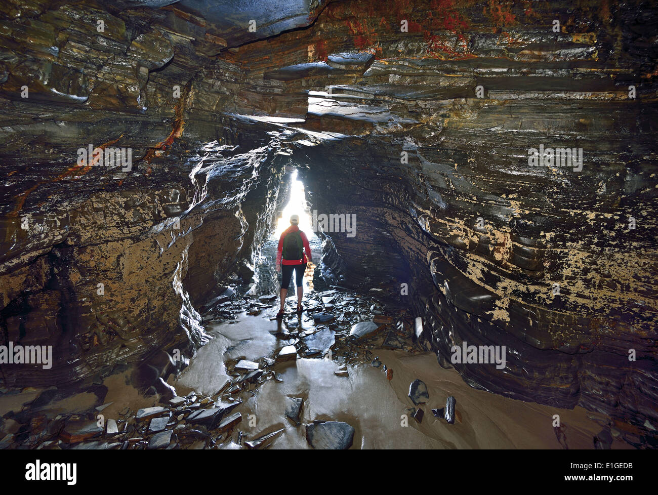 Spain, Galicia, Praia das Catedrais, Playa de las Catedrales, Cathedral s beach, woman, rocky cave, cave, inside, woman crossing rock cave, coast, coastal, beach, national nature monument, travel, tourism, geology, stones, low tide, sand Stock Photo