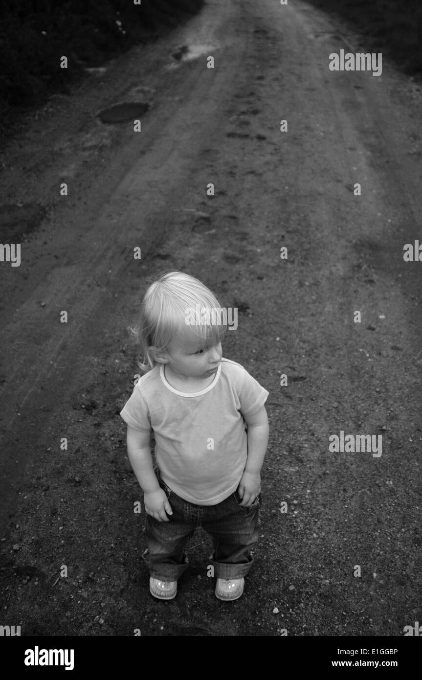 Young toddler girl standing on a dirt track road looking to one side. Stock Photo