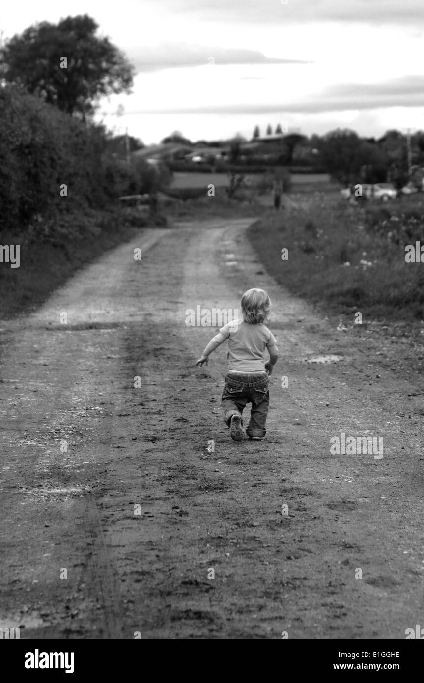 young toddler walking down a dirt track road in the countryside Stock Photo