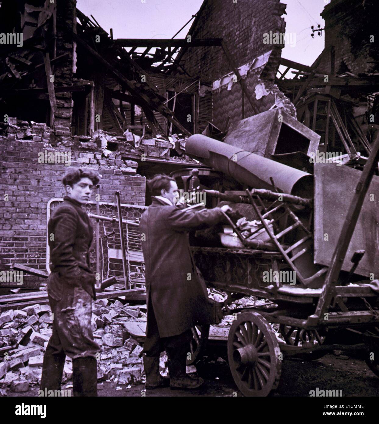 Two men load a wagon with their possessions, among ruins. Stock Photo