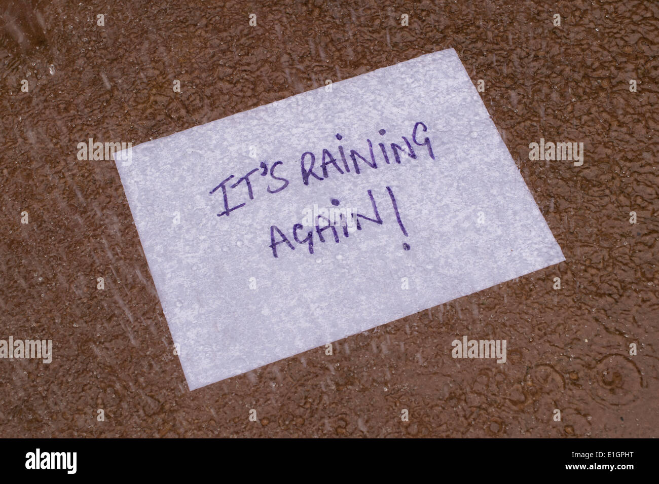 Its Raining Again written on a piece of paper in a puddle in the rain Stock Photo