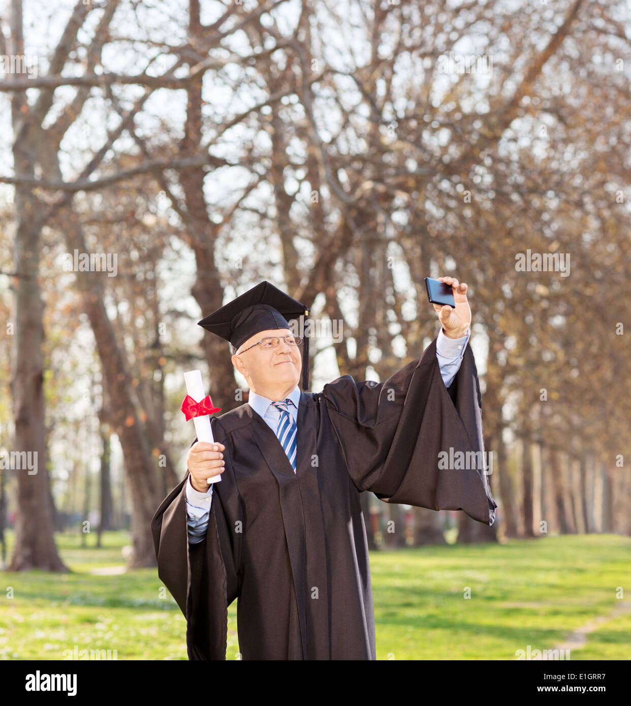 Mature man holding diploma and taking selfie in park Stock Photo