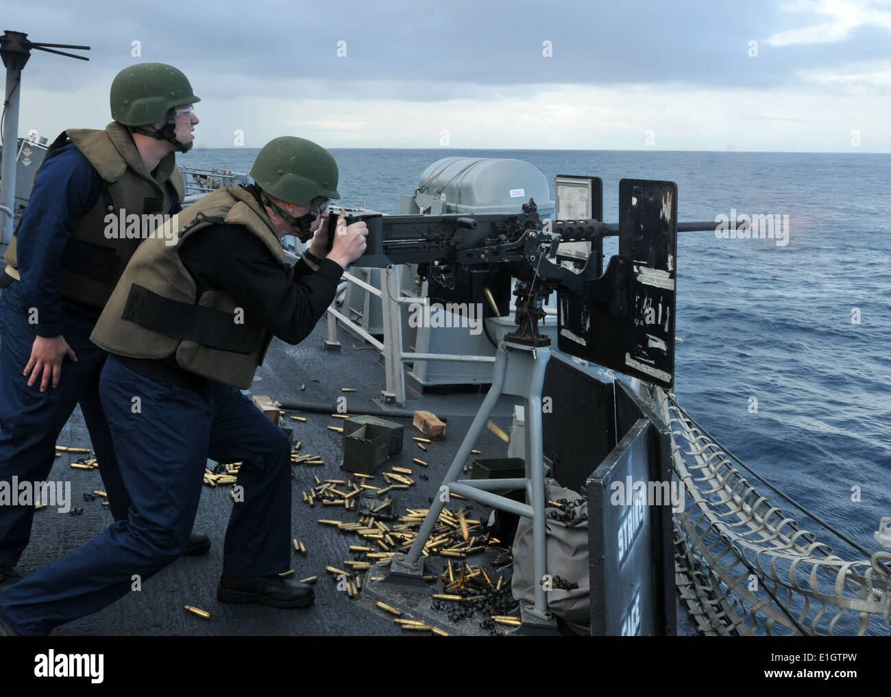 U.S. Navy Midshipman 2nd Class Alex Nestle, right, fires a .50-caliber machine gun aboard the guided missile frigate USS Thach Stock Photo