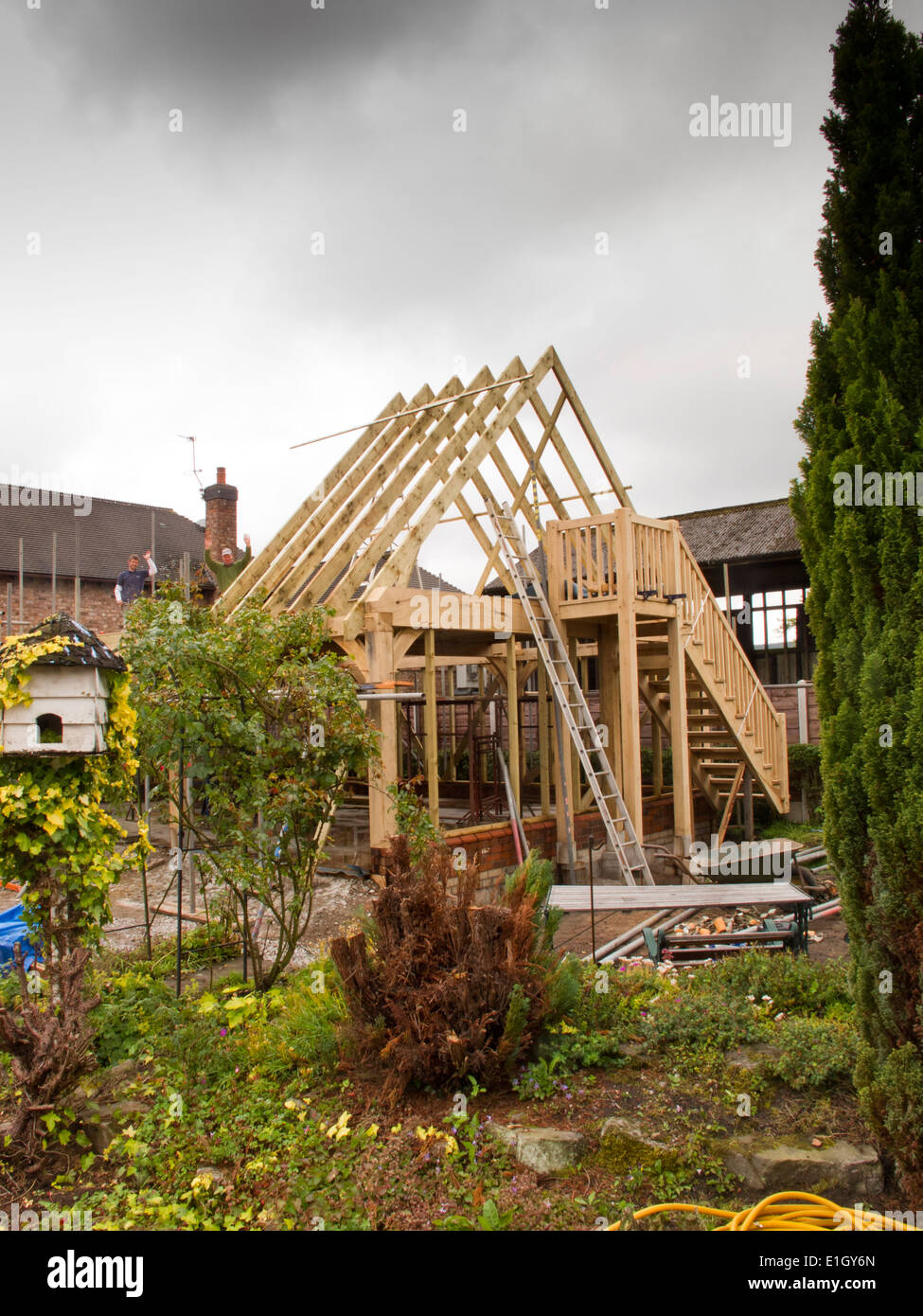 self building house, erecting green oak structure, fixing roof spars with grey rain clouds overhead Stock Photo