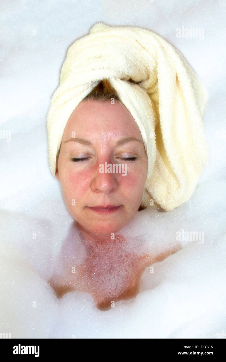 Mature woman surrounded by bubbles in during a luxurious bubble bath Stock Photo