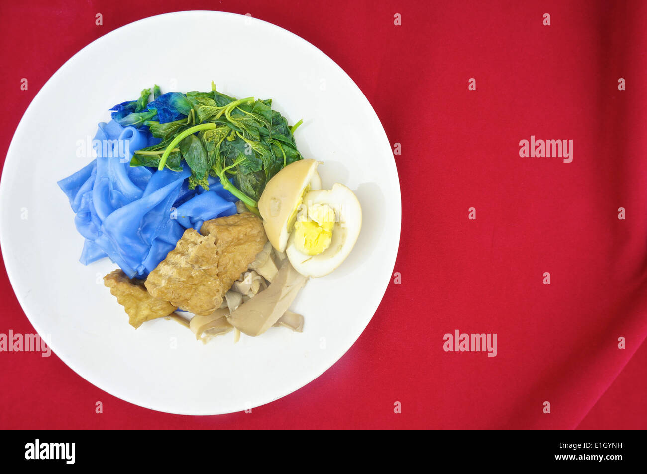 Blue rice noodle with fried tofu, spinach, abalone mushroom and egg boiled in the gravy vegetarian on red background. Stock Photo