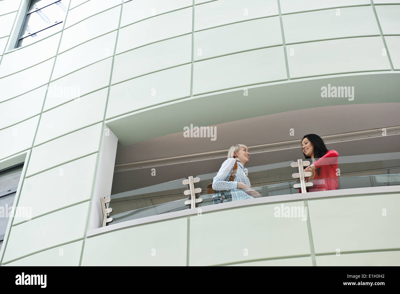 Two young women talking on balcony, low angle Stock Photo