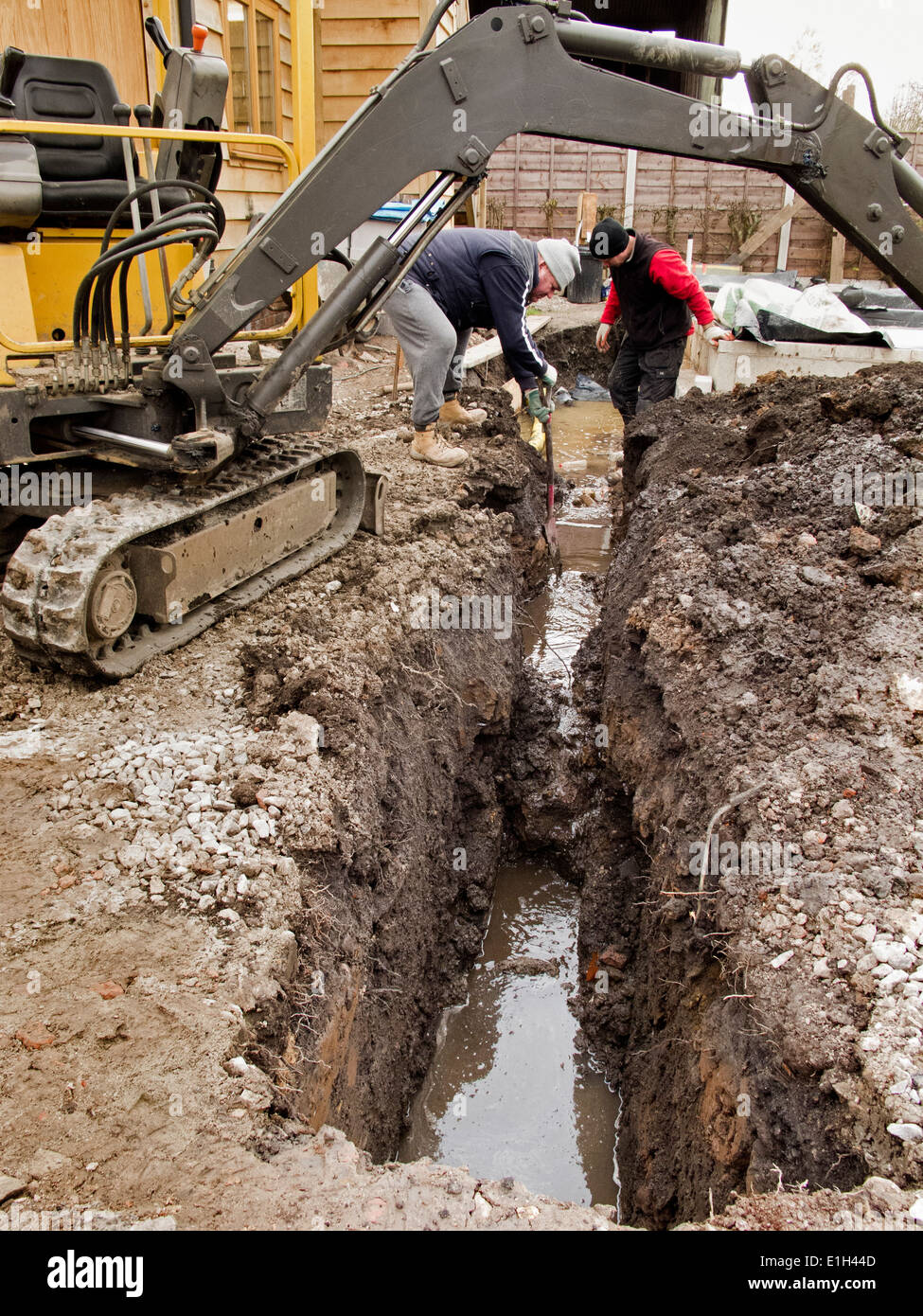 self building house, men excavating ditches for drains with mini digger excavator machine Stock Photo