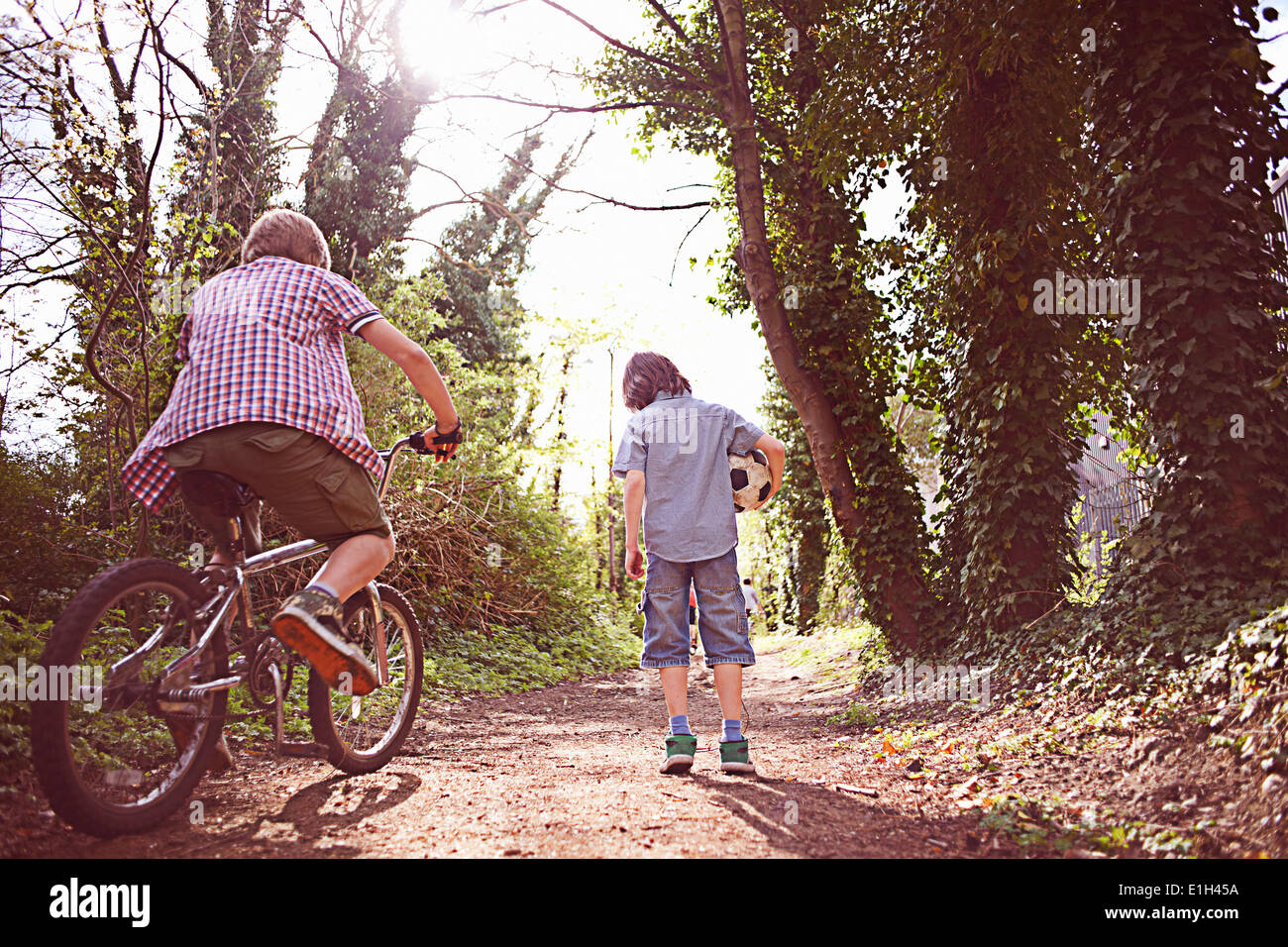 Boy on bike with friend on forest path Stock Photo
