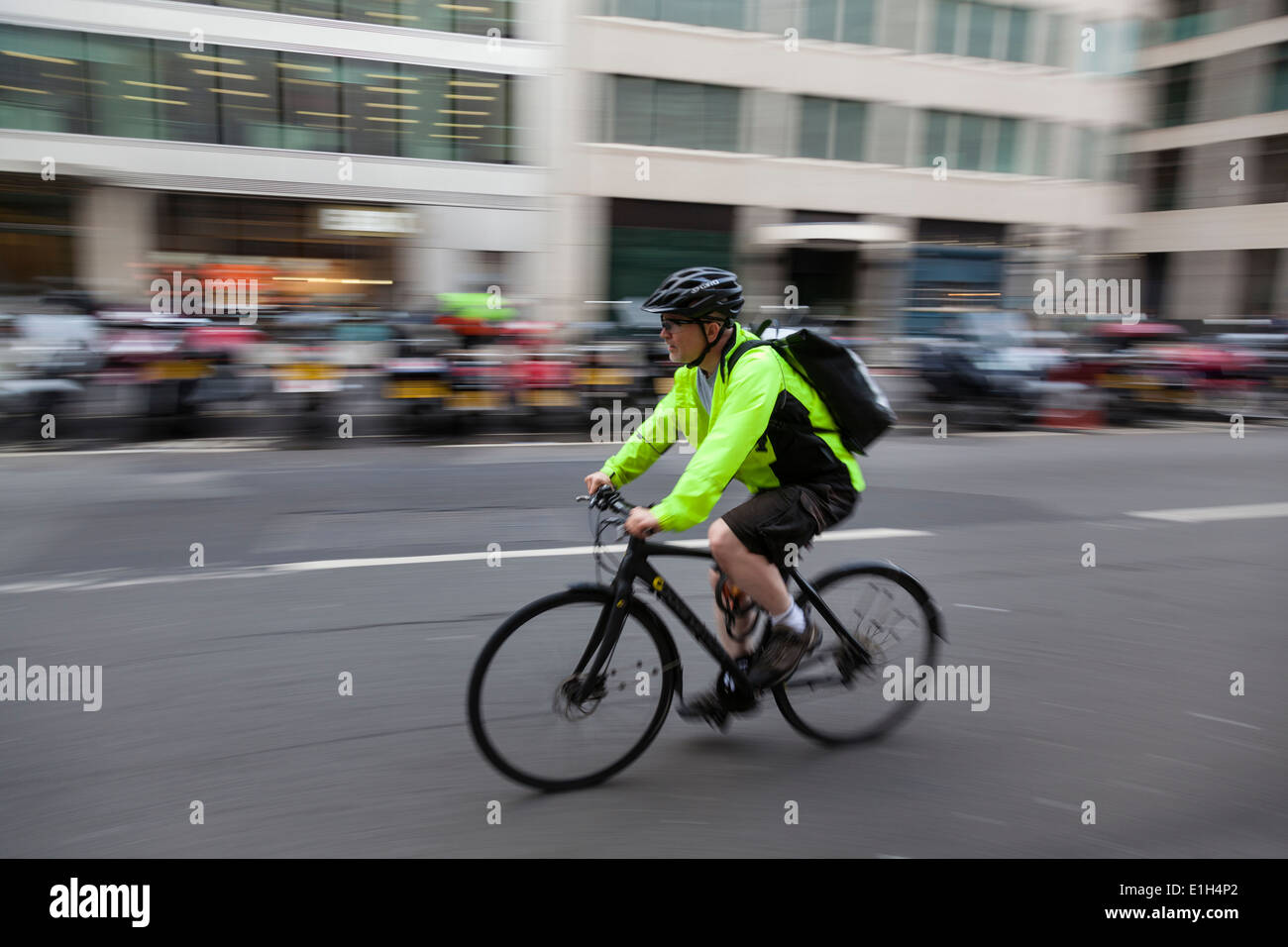 Man wearing a yellow hi-viz jacket, helmet and backpack rides his mountain bike along a London street. Stock Photo