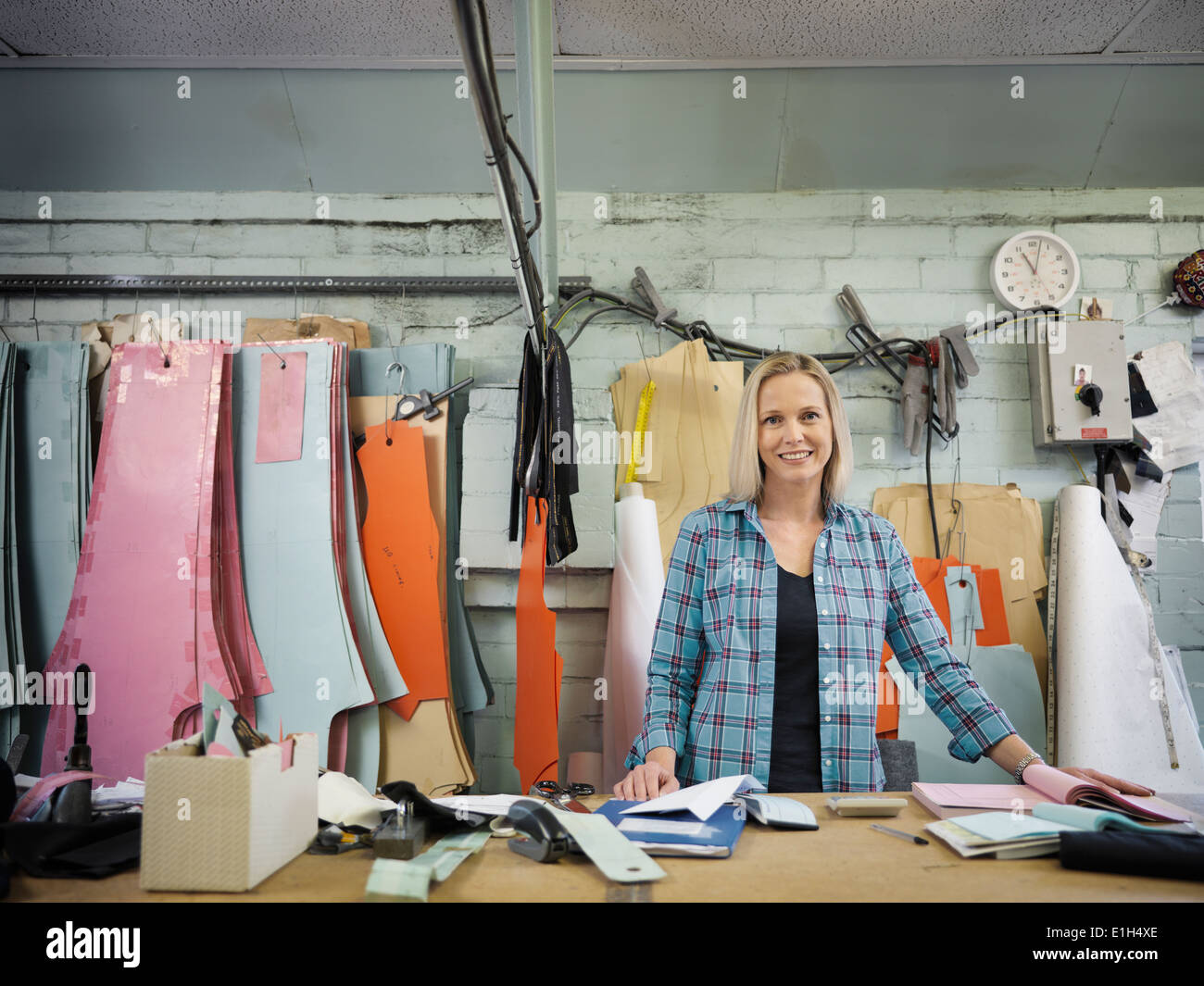 Portrait of fashion designer at cutting desk in clothing factory, smiling Stock Photo