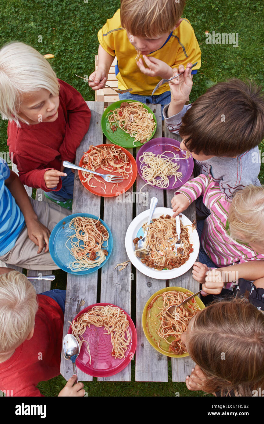 Overhead view of seven children eating spaghetti at picnic table Stock Photo