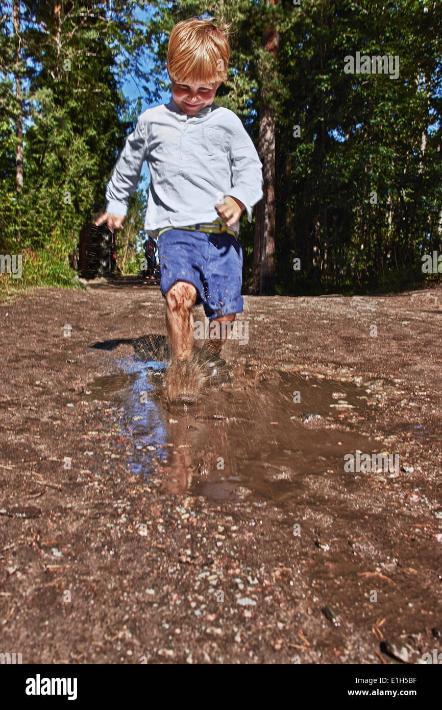 Young boy splashing in muddy puddle Stock Photo