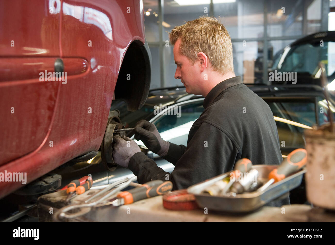 A mechanic in a garage is checking and repairing the brakes of a lifted car. Stock Photo