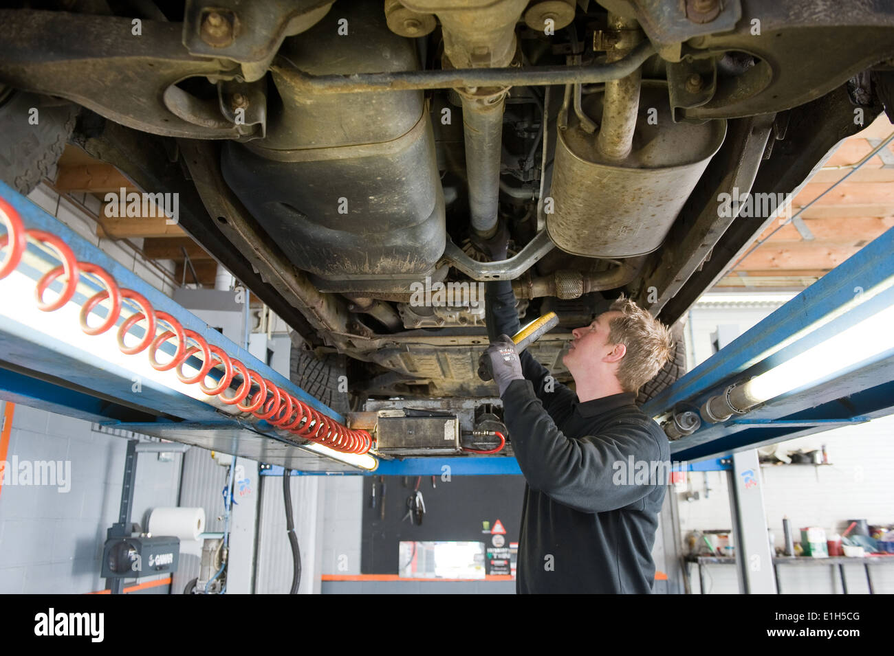 A mechanic is checking the technical state underneath a lifted car on a bridge in a garage. Stock Photo