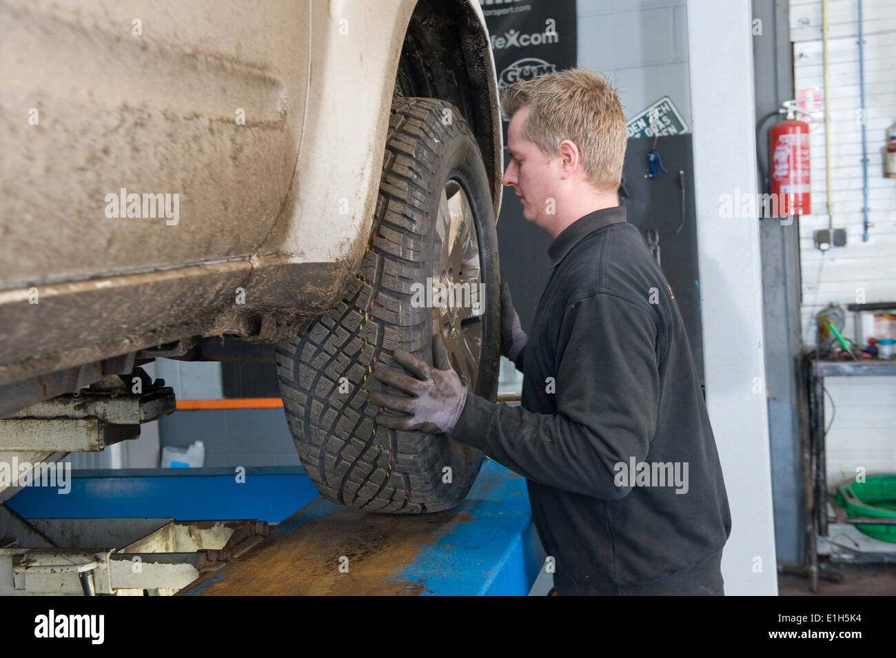 A mechanic is changing the wheel of a lifted car on a bridge in a garage. Stock Photo