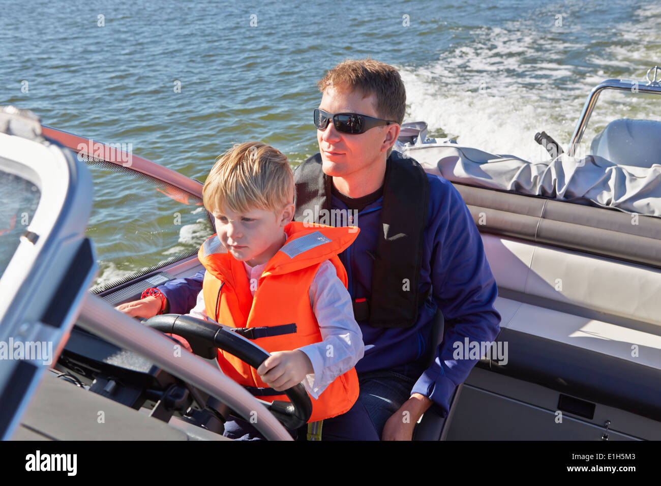 Young boy sitting on fathers lap steering motor boat Stock Photo