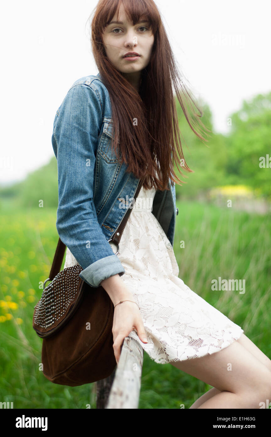 Portrait of young woman sitting on fence in field Stock Photo