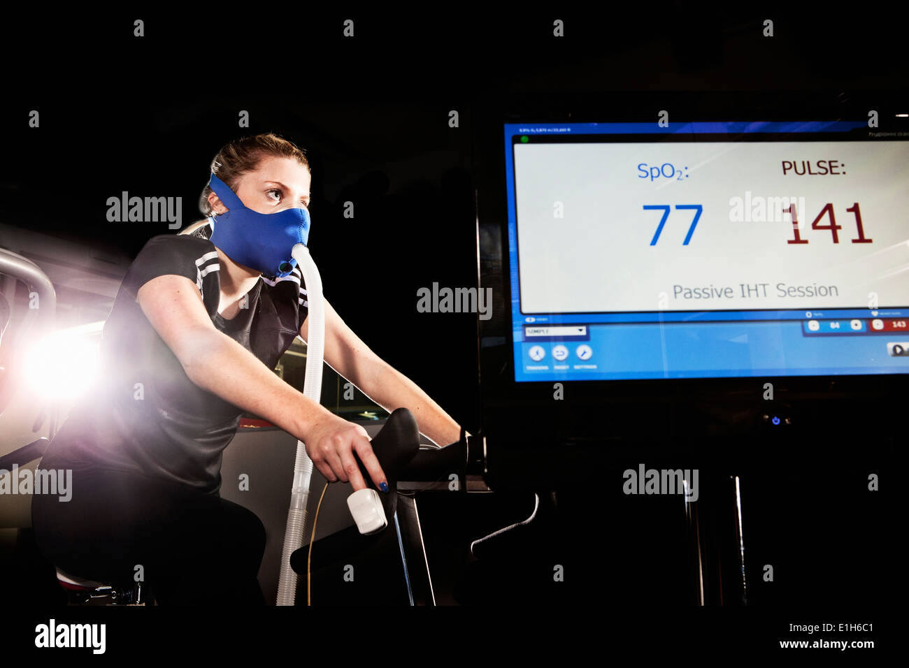 Young woman in face mask on gym exercise cycle in altitude centre Stock Photo