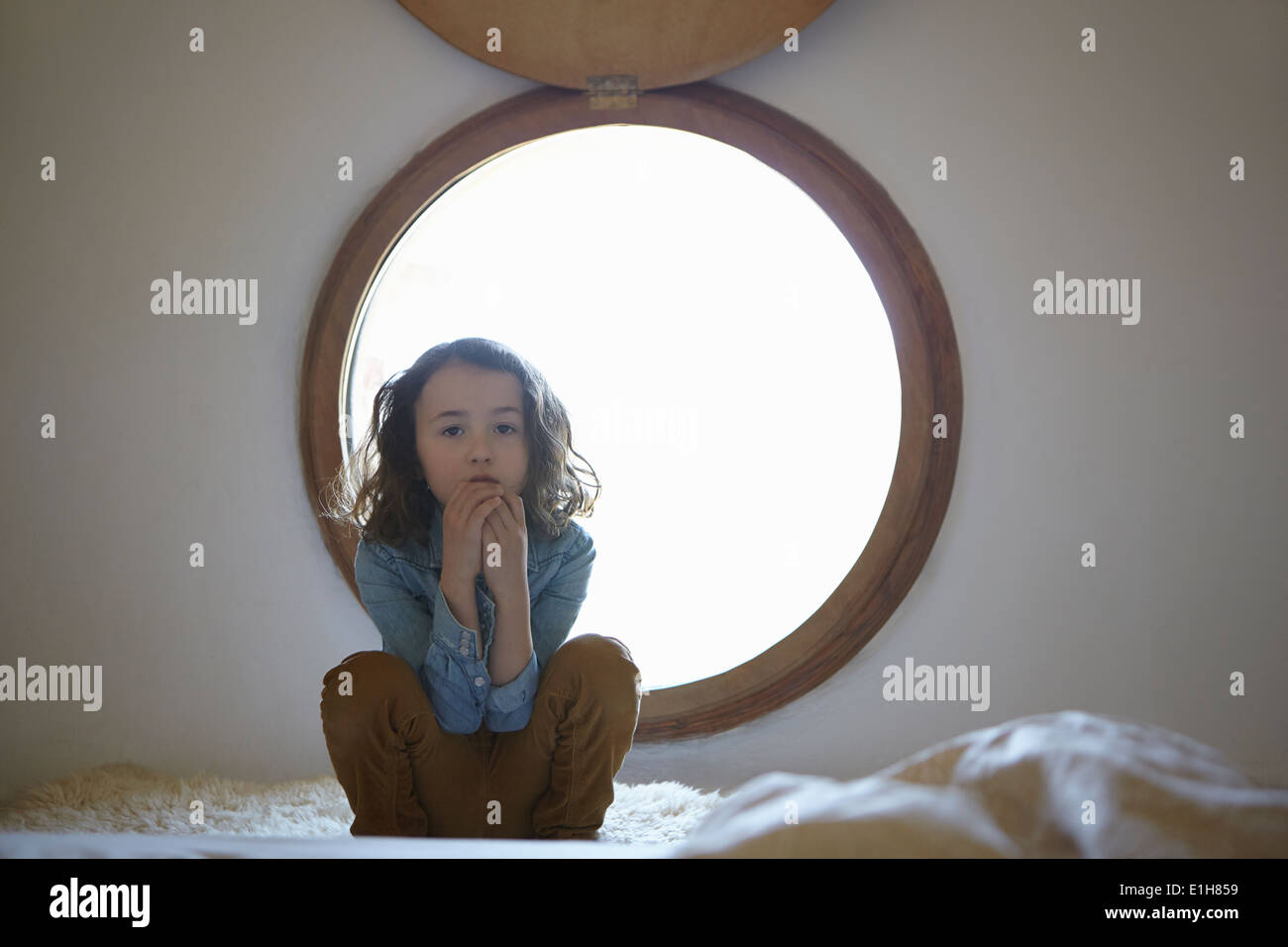 Portrait of sullen girl crouching in front of circular window Stock Photo