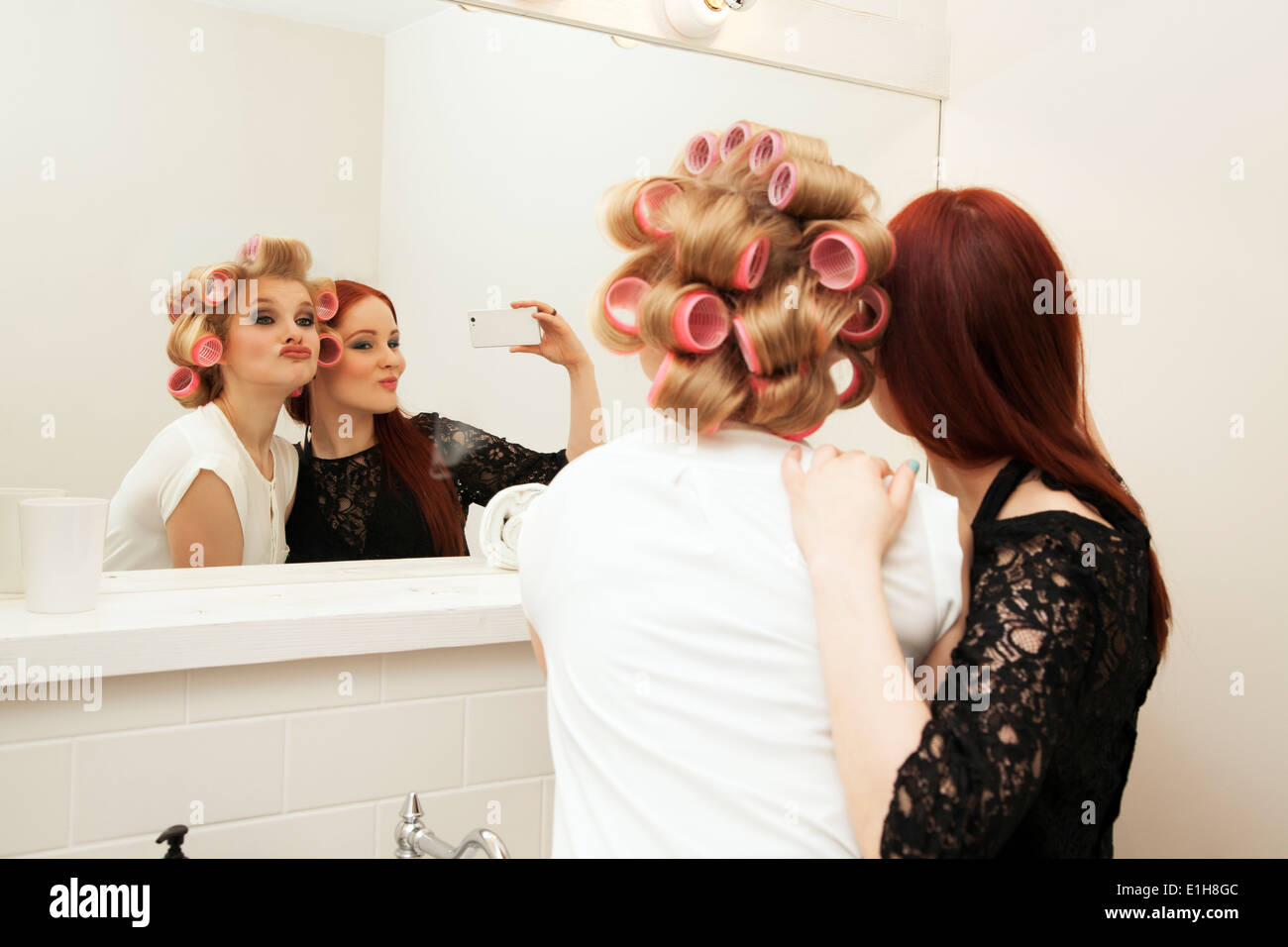 Young woman in curlers and friend taking selfie Stock Photo
