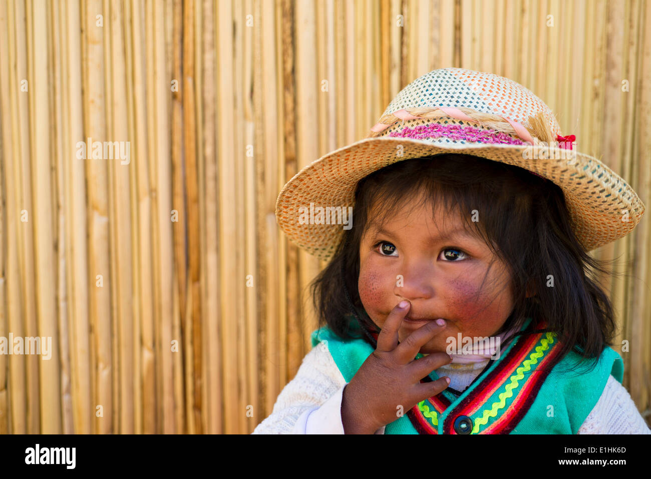 Young girl of the Uro Indians, about 6 years old, wearing traditional dress in front of a reed hut, floating islands made of Stock Photo