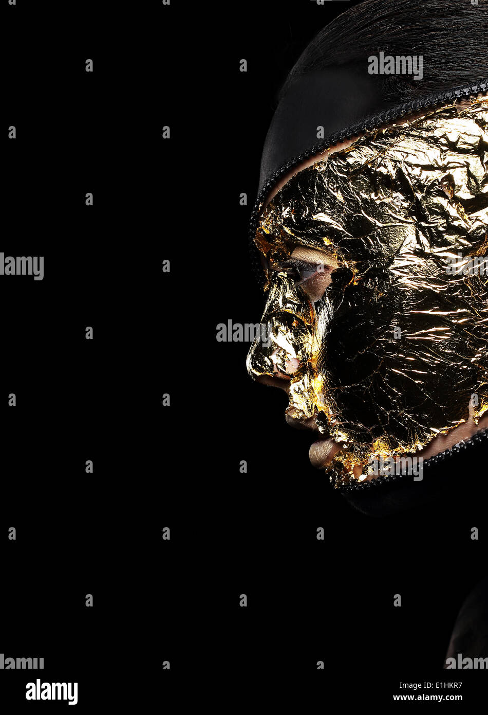 Styled Woman's Face Covered Golden Foil over Black Background. Mystery Stock Photo