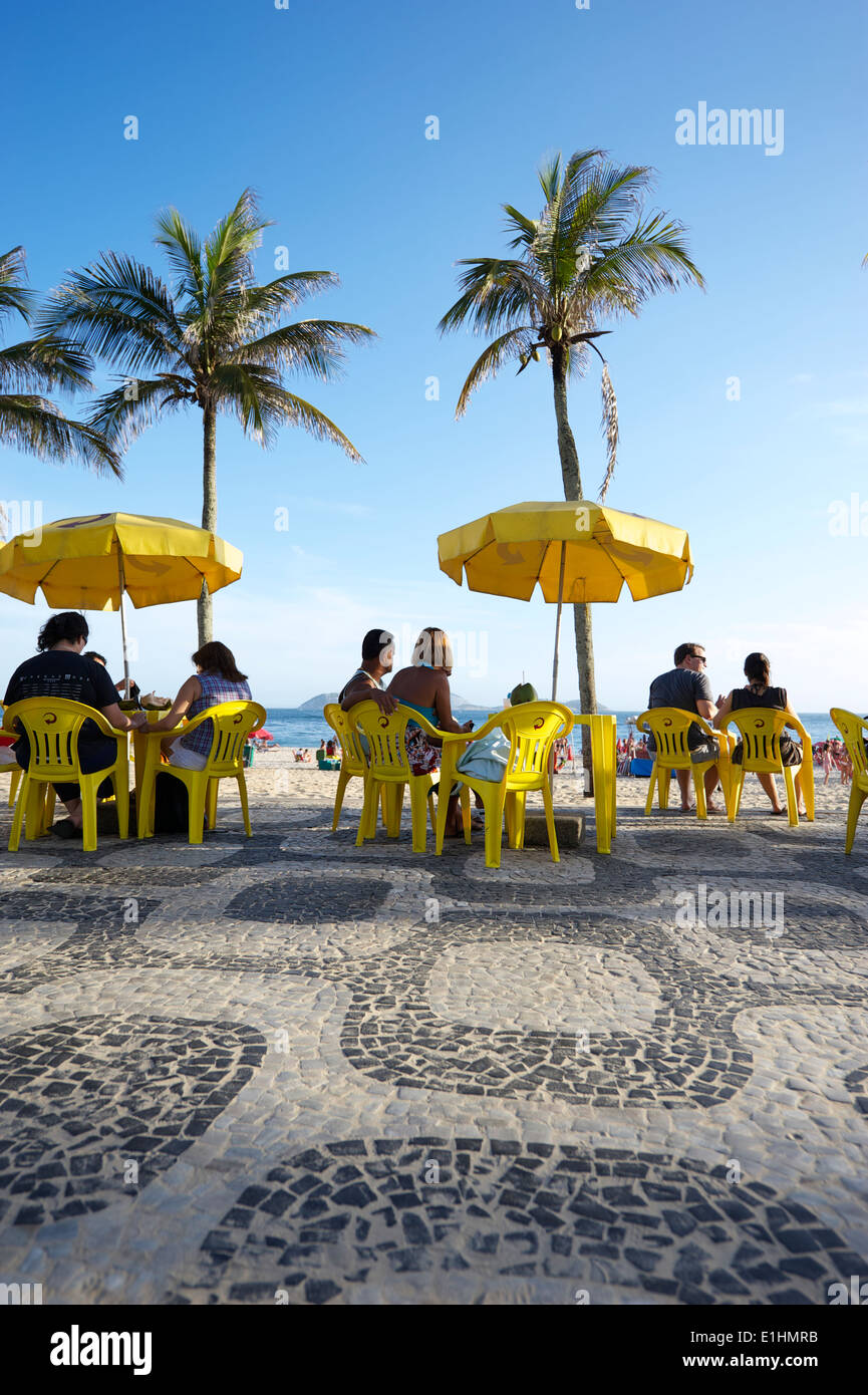 RIO DE JANEIRO, BRAZIL - JANUARY 19, 2014: People relax in collection of yellow chairs and tables at a kiosk on the boardwalk. Stock Photo