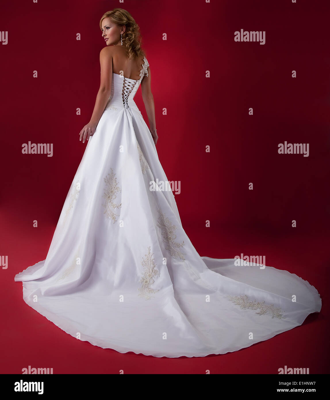 Fashionable blonde young bride in long white wedding dress over red background. Studio shot Stock Photo