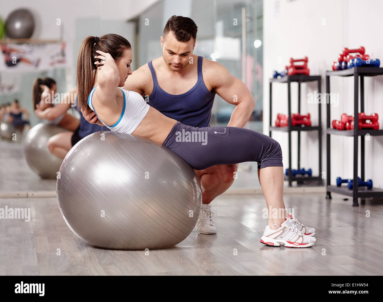 Personal trainer helping woman doing abs crunches with gym ball Stock Photo