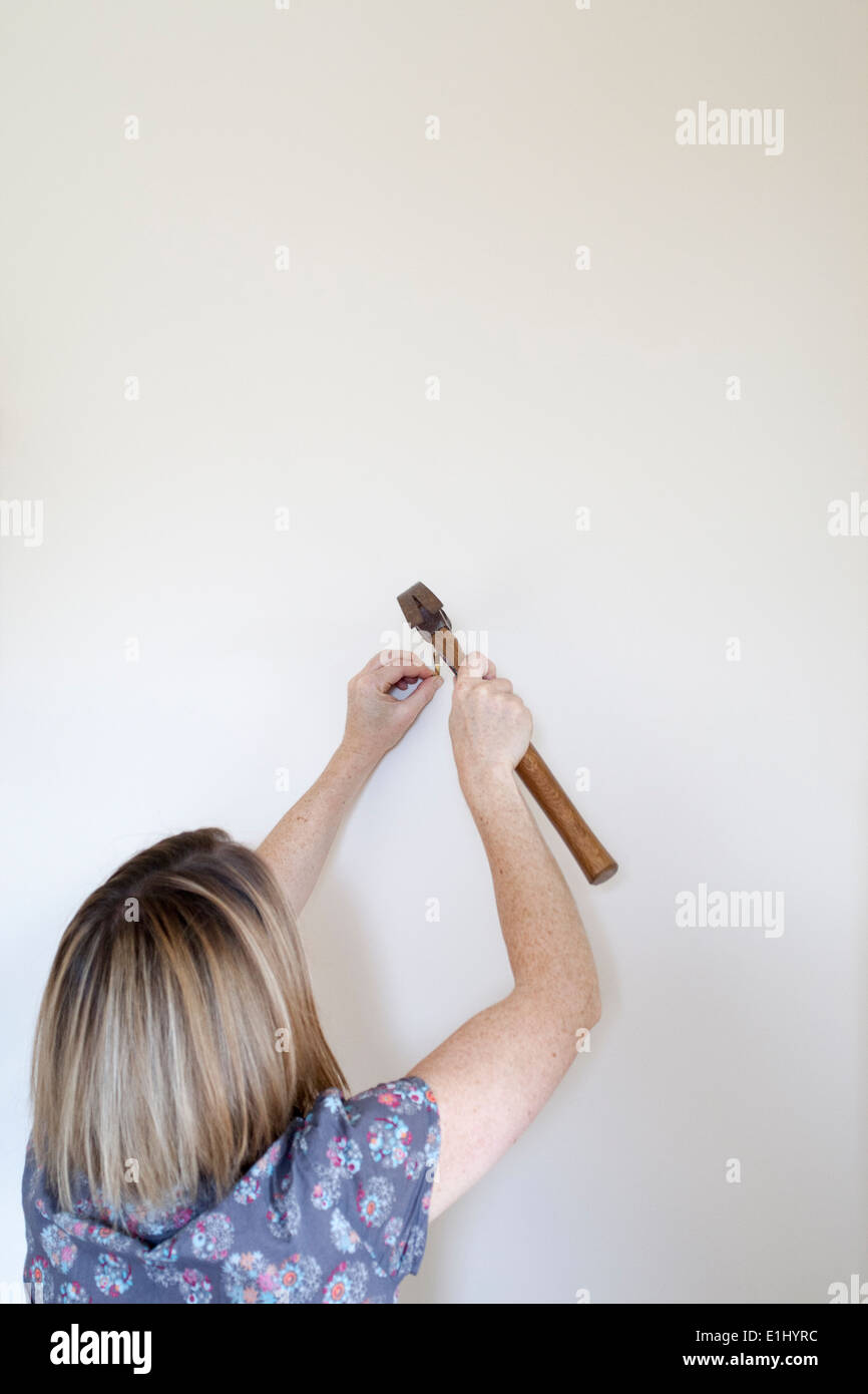 30-35 woman hammering a picture hook into the wall Stock Photo