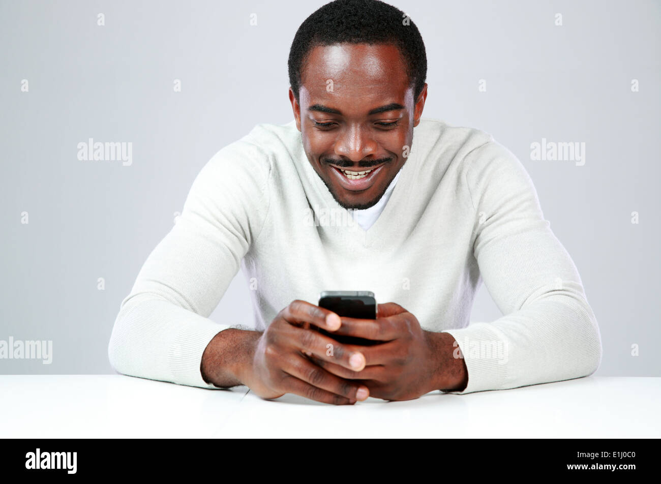 Happy african man sitting at the table and using smartphone Stock Photo