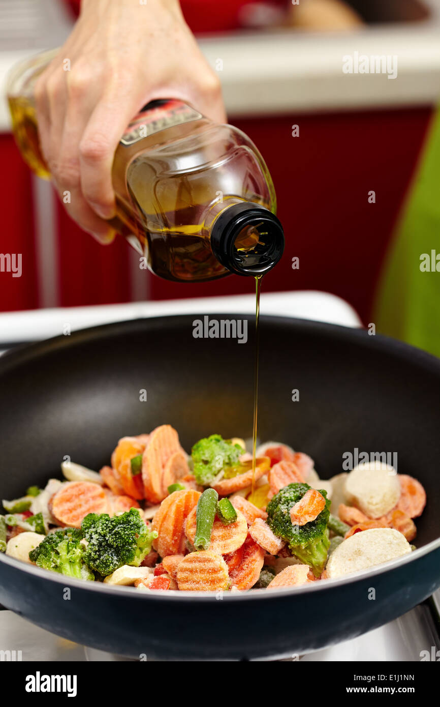 Closeup of woman's hand pouring olive oil over frozen vegetables in the