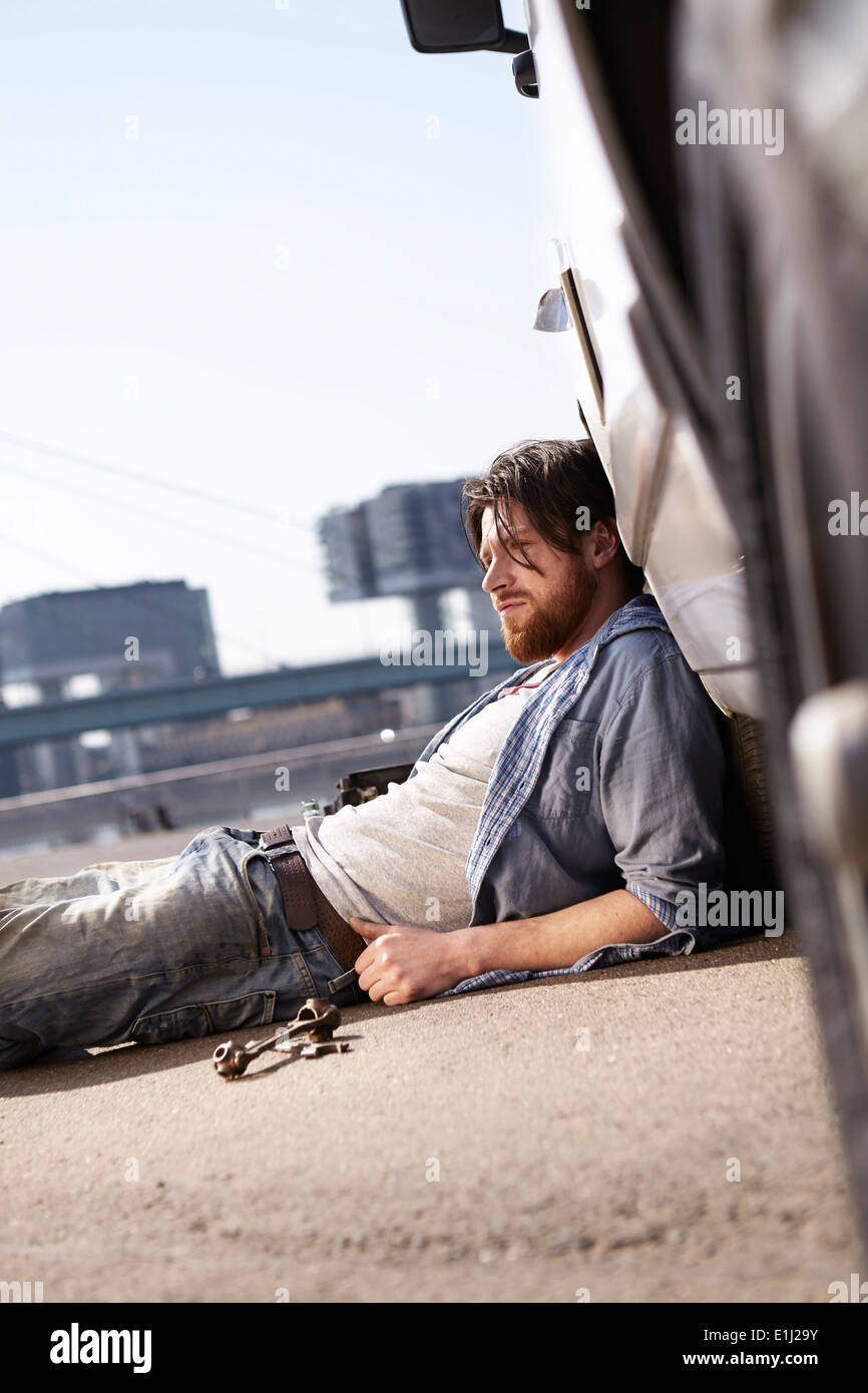 Man lying on ground leaning against car Stock Photo