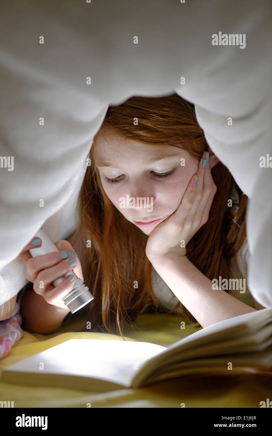Portrait of girl reading a book secretly in bed under the blanket Stock