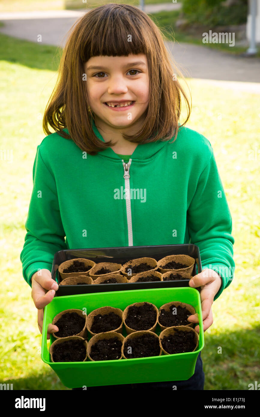 Portrait of little girl holding plastic boxes with nursery pots Stock