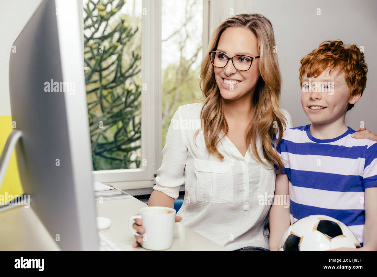 Mother and son with soccer ball at desk with computer Stock Photo