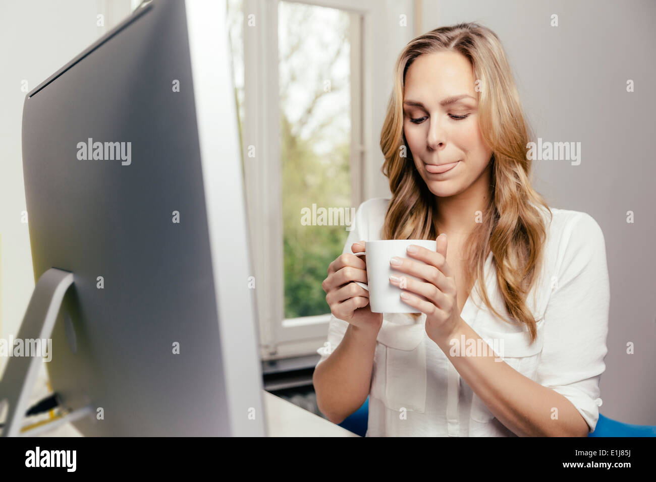 Blond young woman at desk drinking cup of coffee Stock Photo