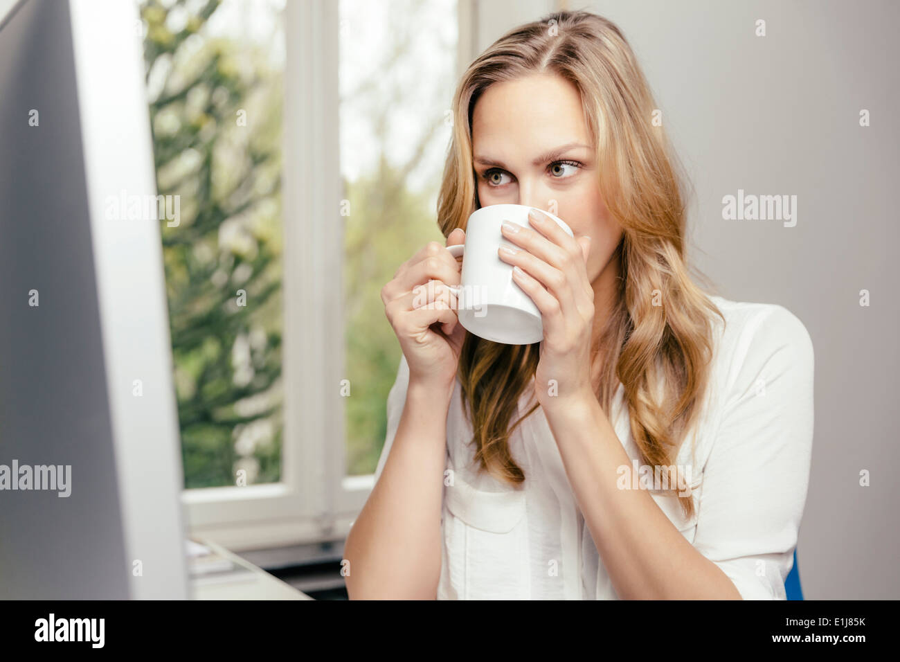 Blond young woman at desk drinking cup of coffee Stock Photo