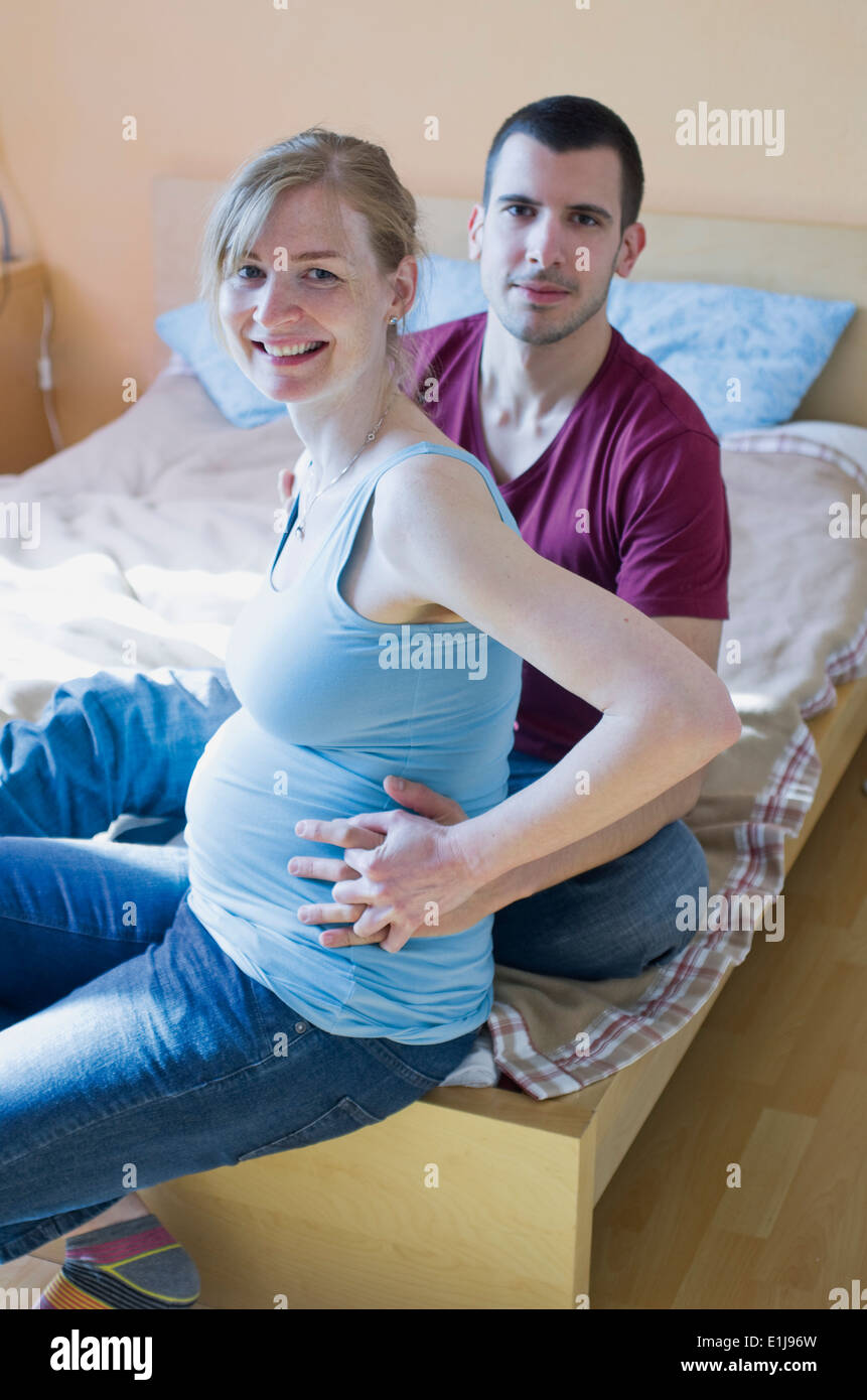 Couple expecting a baby sitting on bed at home Stock Photo