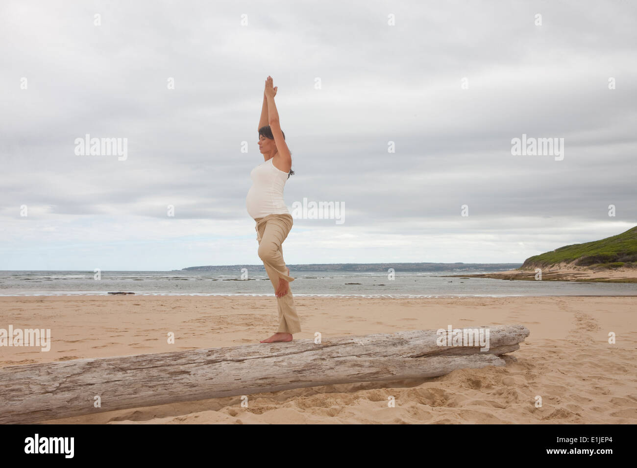 Pregnant mid adult woman practicing yoga on tree trunk at beach Stock Photo