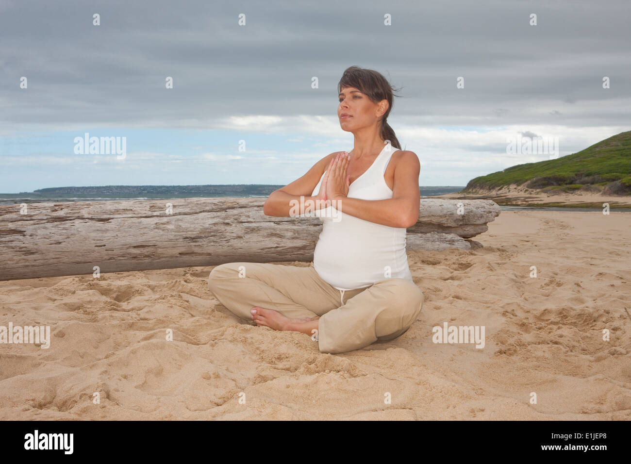 Pregnant mid adult woman practicing yoga on beach Stock Photo