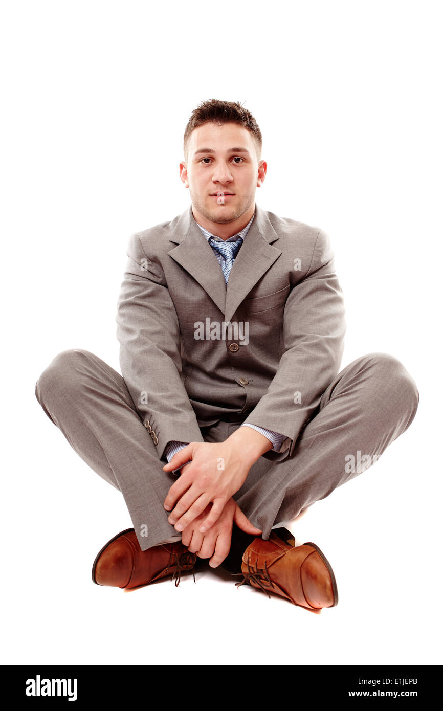 Studio portrait of young positive businessman sitting cross legged ...
