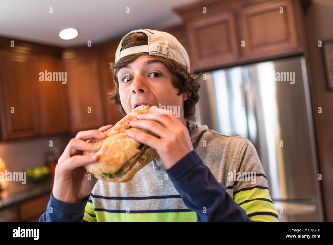 Teenage boy in kitchen biting large sandwich Stock Photo