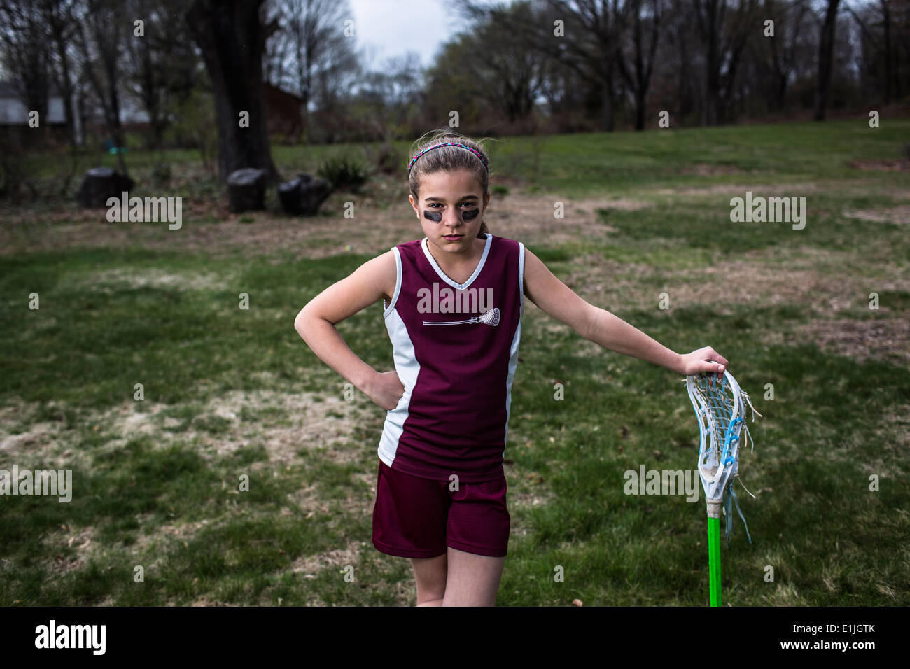Girl wearing lacrosse uniform, leaning against lacrosse stick Stock