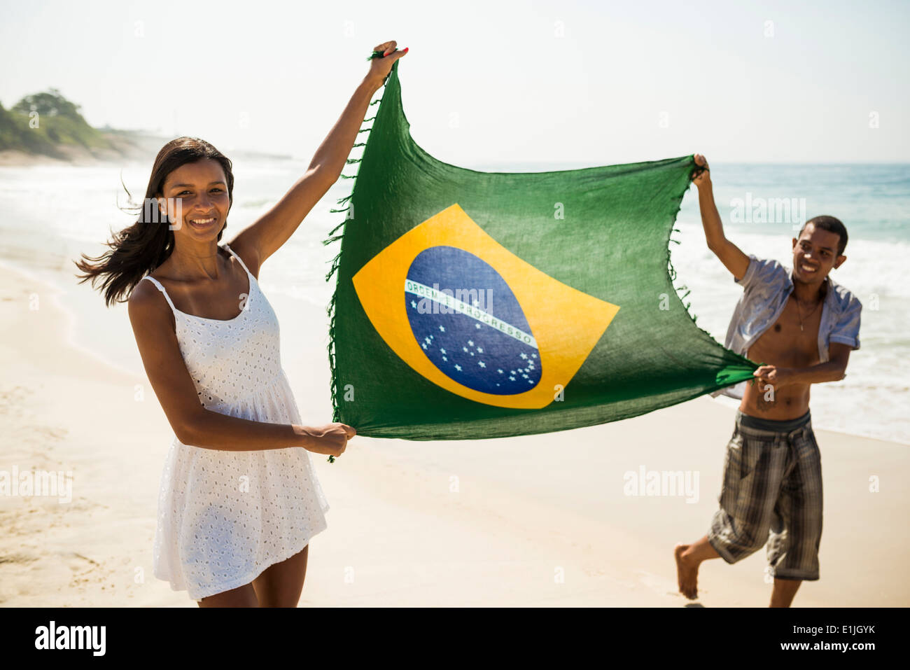 Young couple holding up Brazilian flag, Arpoador beach, Rio De Janeiro, Brazil Stock Photo