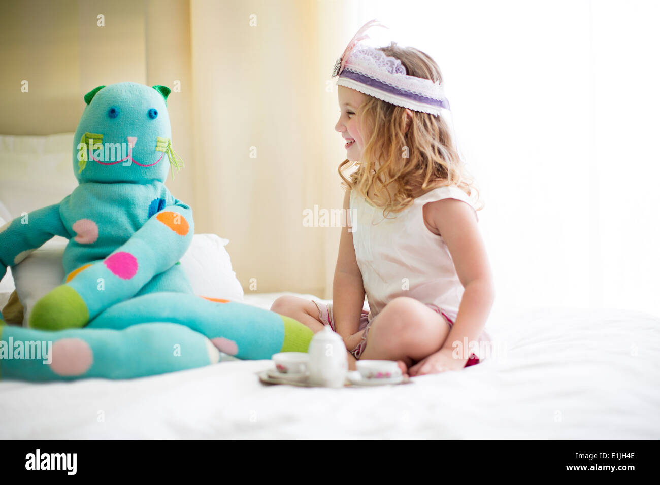 Young girl sharing tea with cuddly toy on bed Stock Photo